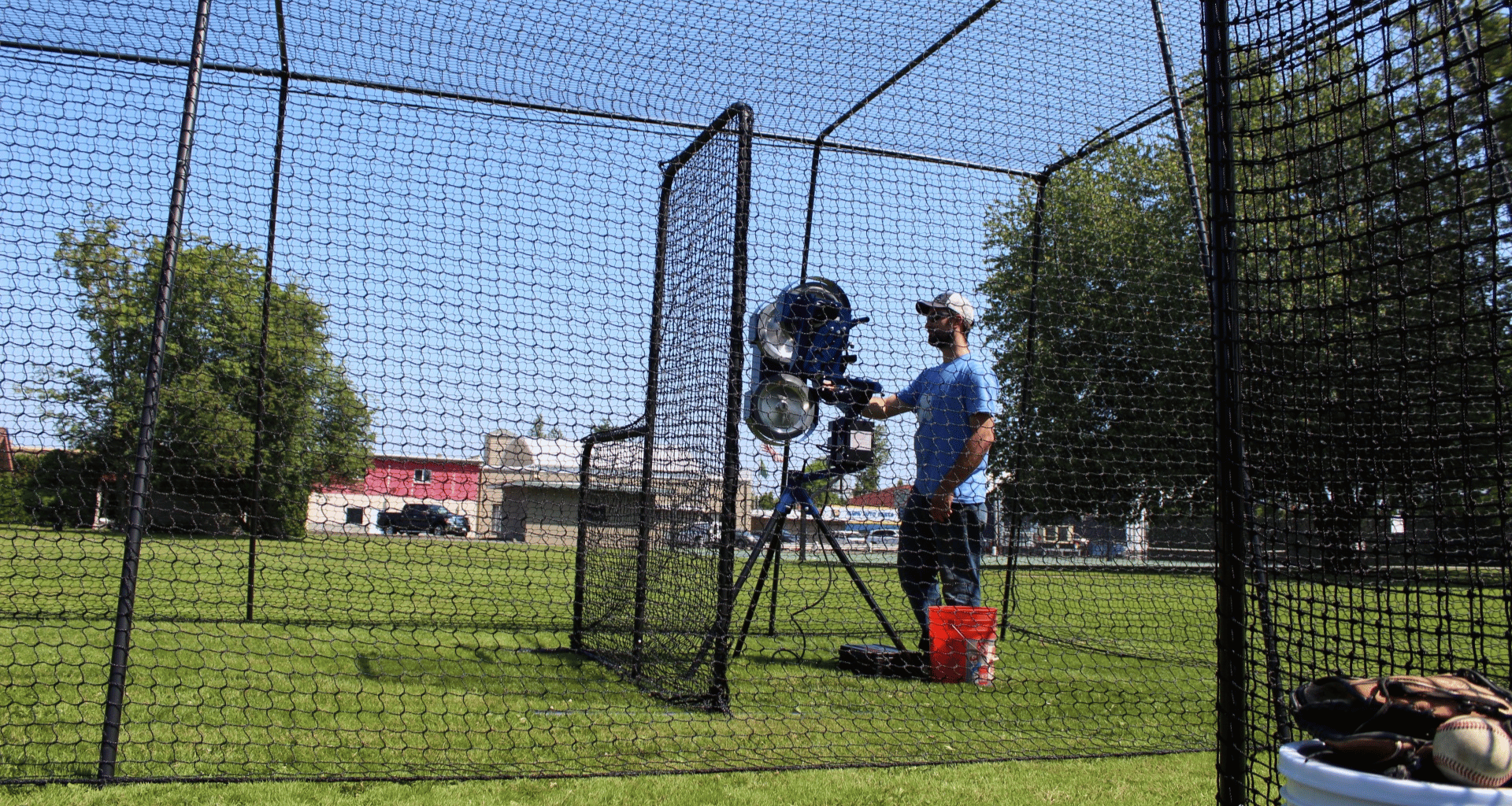 Man feeding the bata 2 pitch 3 pitching machine inside the Trapezoid batting cage