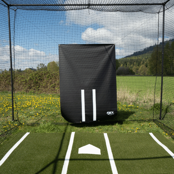 A black vinyl backdrop hung inside a batting cage with a green batters box mat and green grass