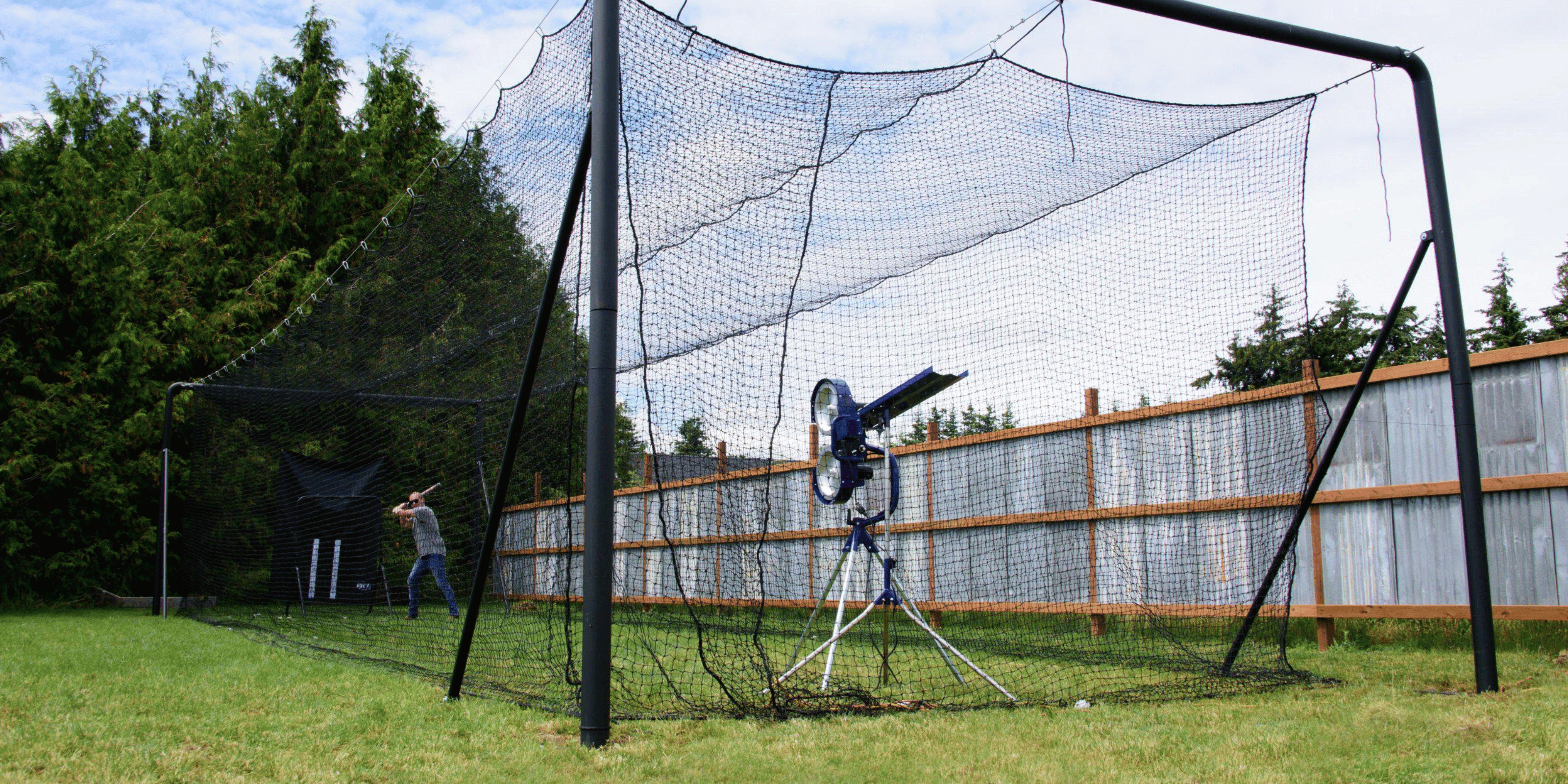 Iron Horse batting cage in a backyard with a man batting baseballs from a bata 2 pitching machine