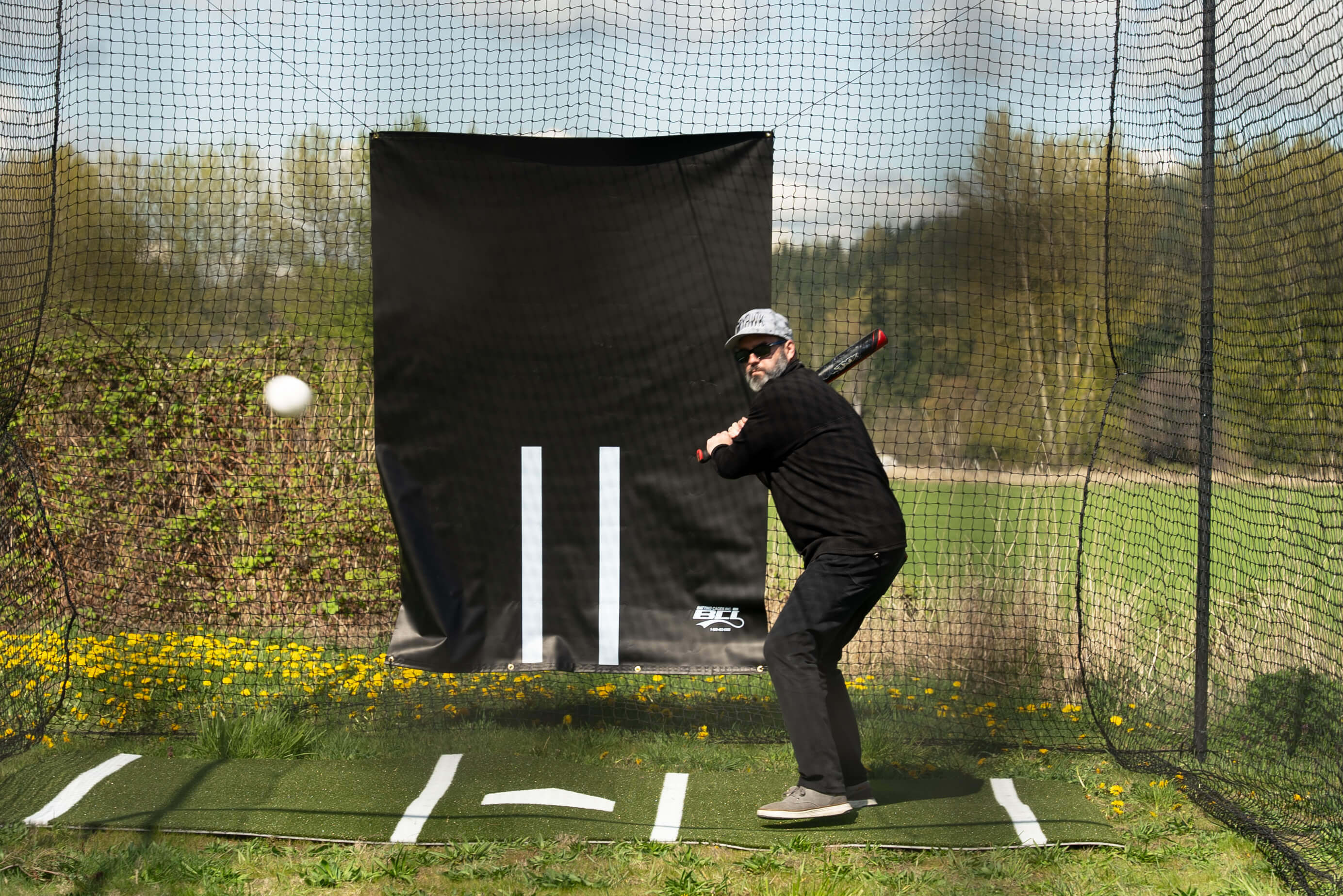 Man batting while standing on a batters box mat and in front of a vinyl backdrop while in the batting cage