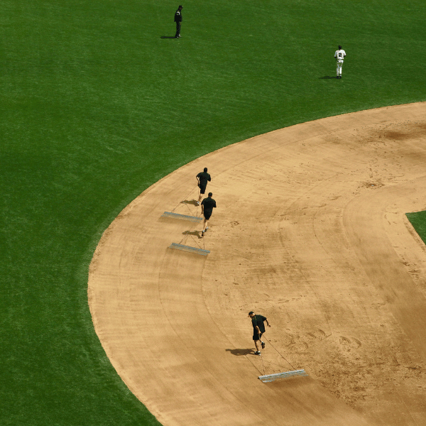 Three men dragging drag mats along the baseball infield