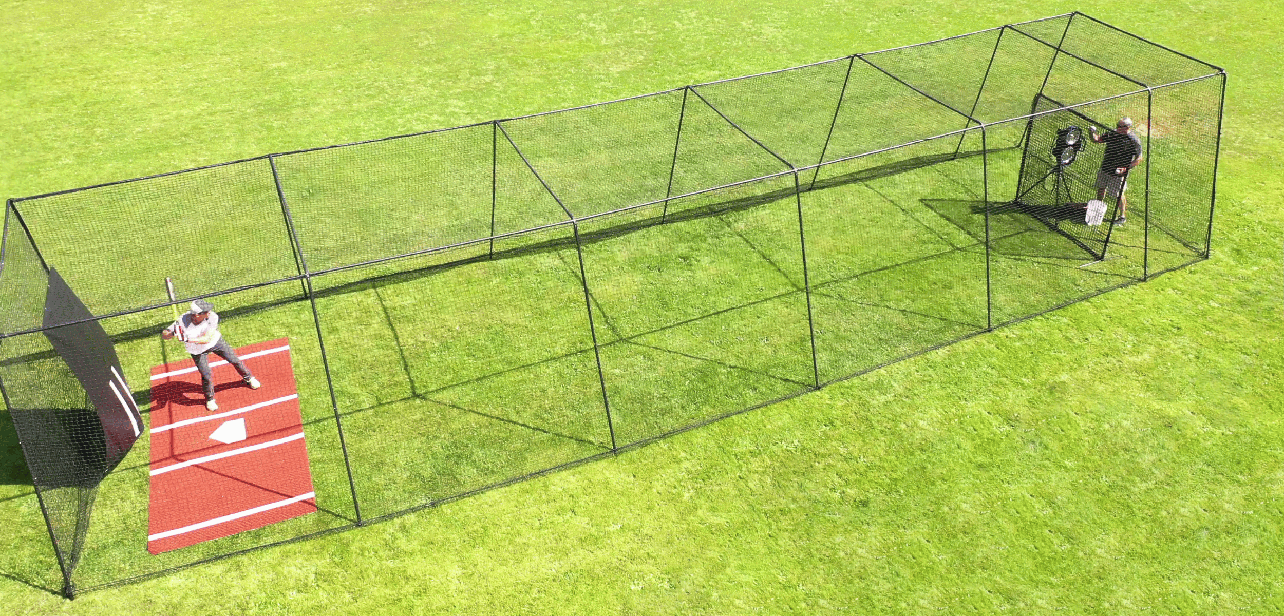 Man batting in Trapezoid batting cage with mat, backdrop, and pitching machinel