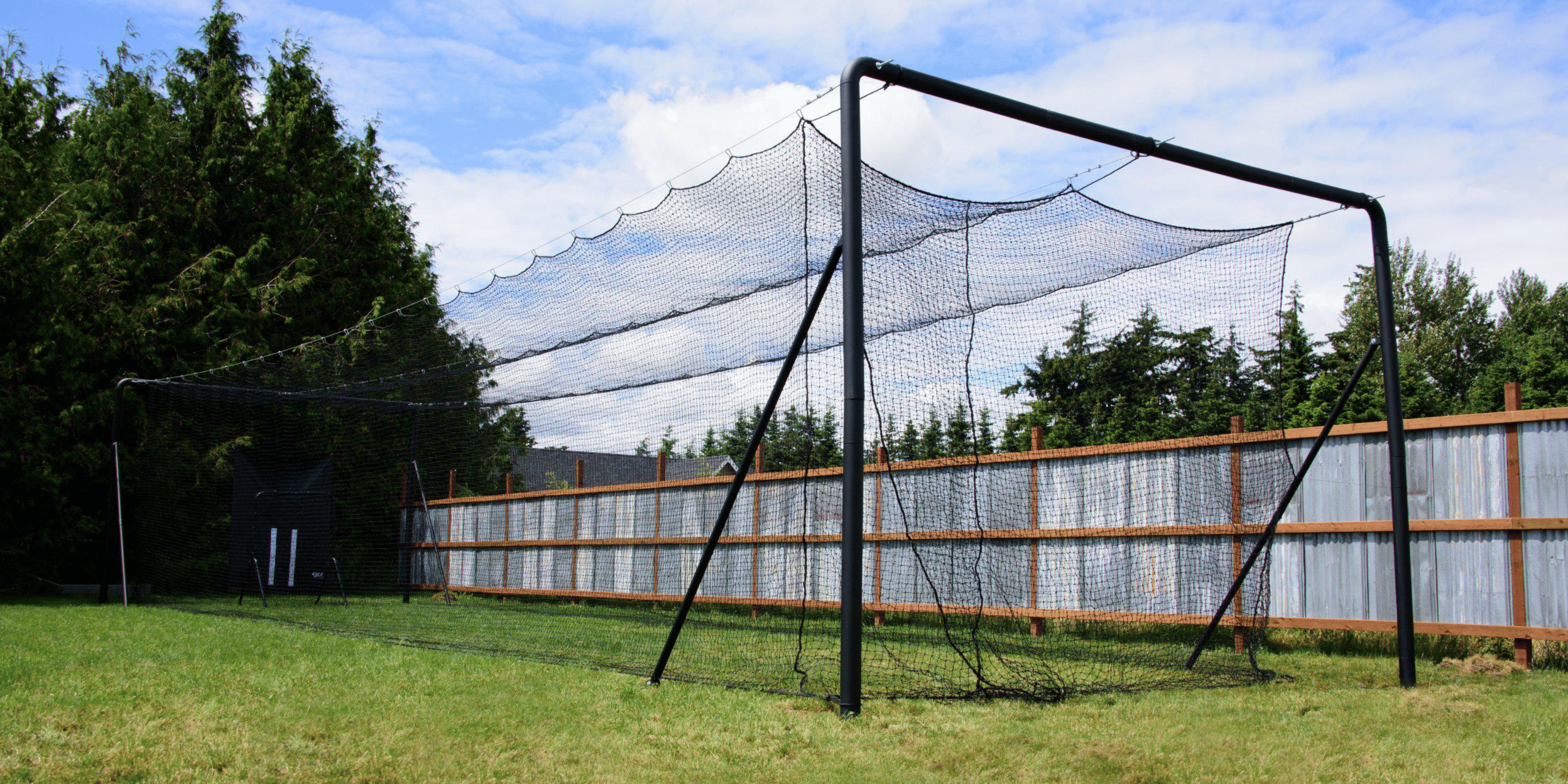 Iron Horse batting cage in a backyard with a fence, trees, and blue skies