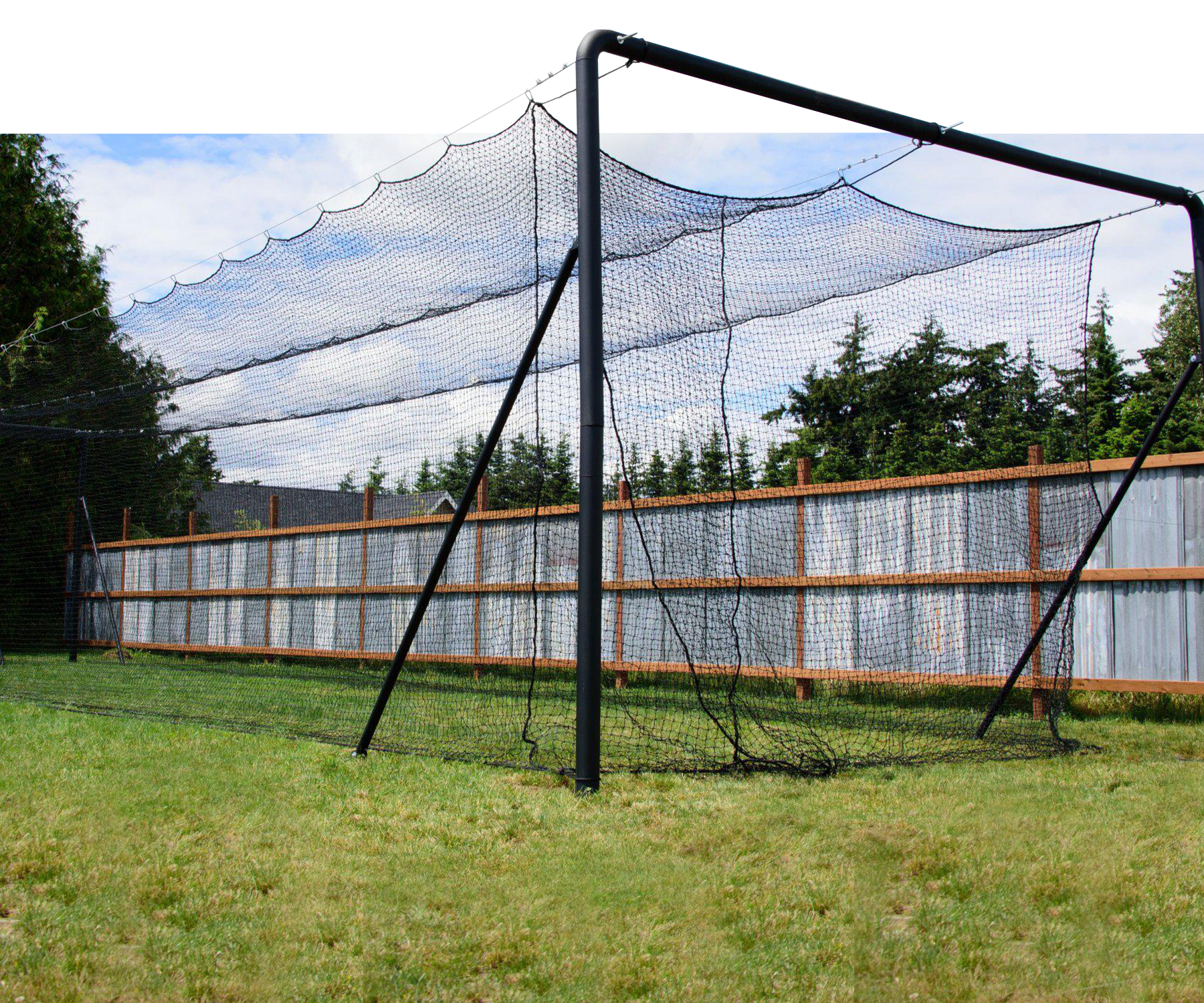 Iron Horse batting cage in backyard with fence, grass, trees, and blue skies