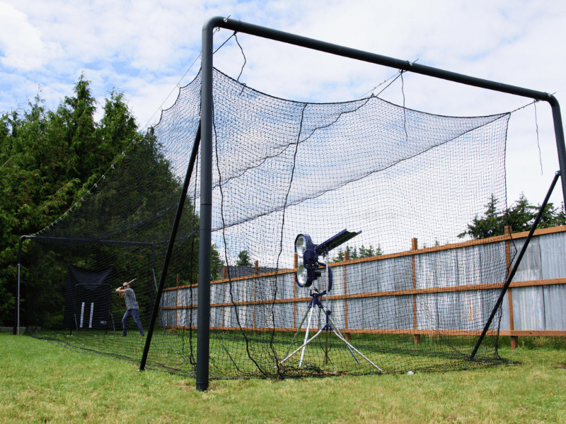 Iron Horse batting cage with man hitting baseballs pitched by a pitching machine in his backyard
