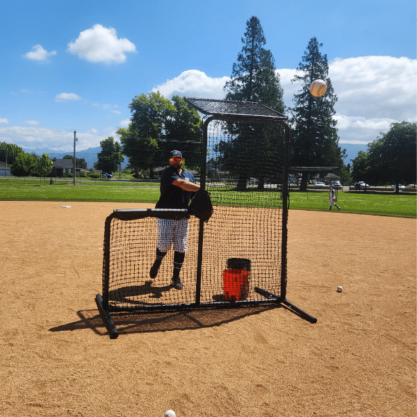 Man throws a baseball while behind the armadillo L-screen on a baseball field