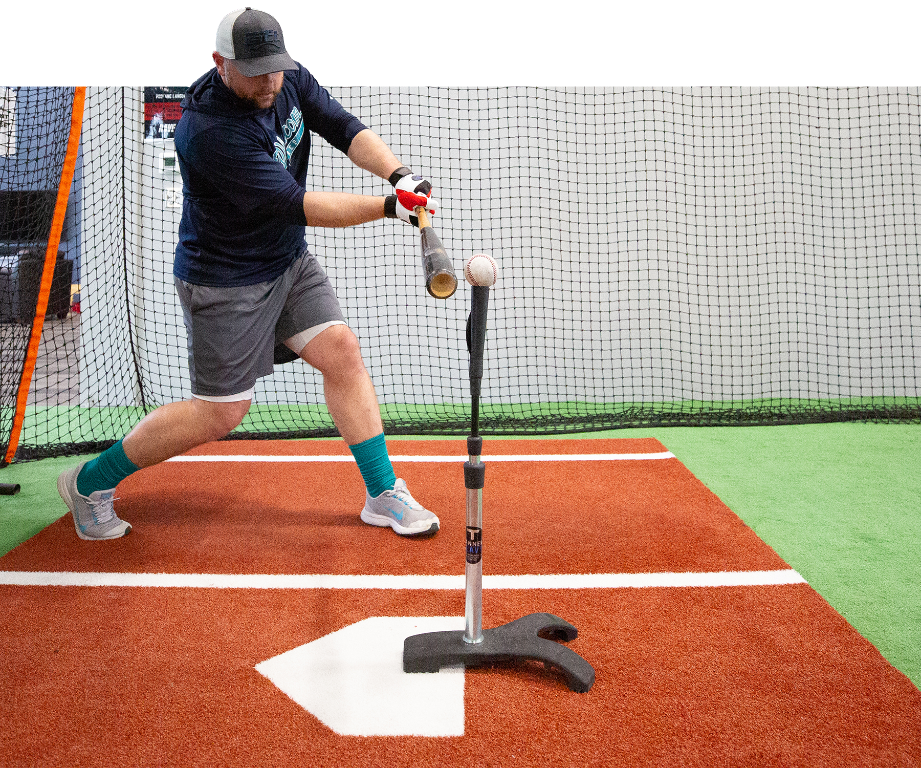 Man hitting baseball off of tanner heavy tee in indoor facility