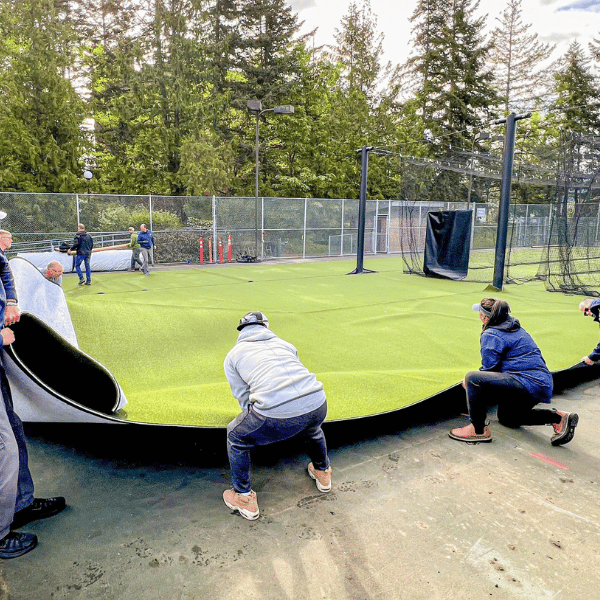 Men and women positioning turf in outdoor batting cage court