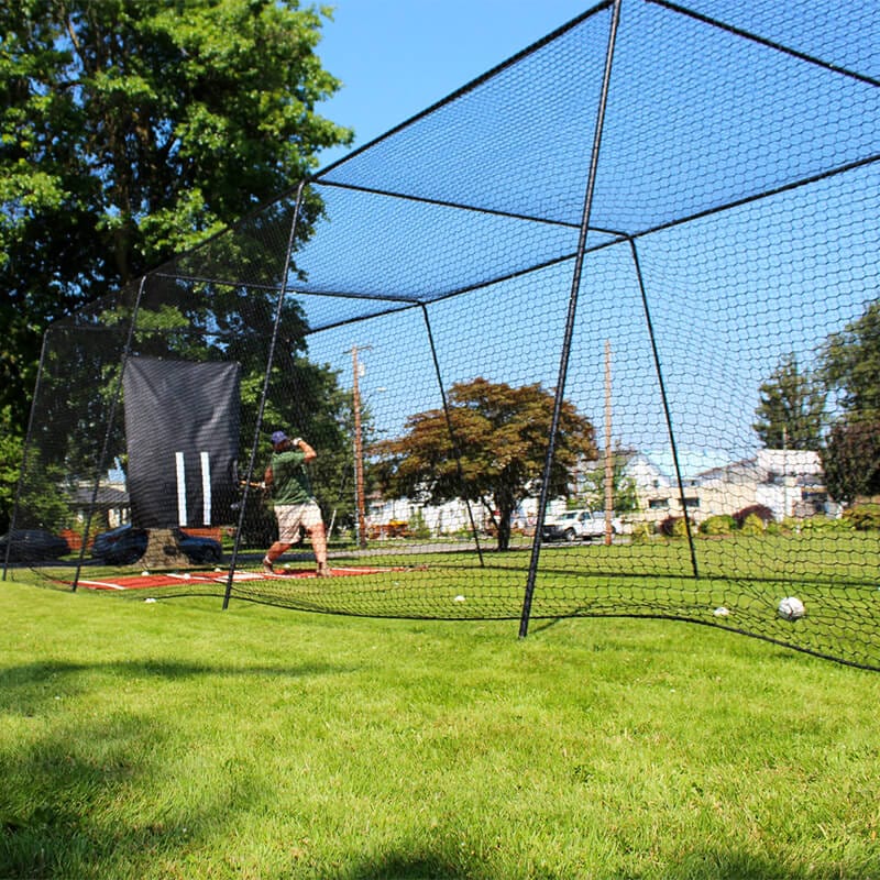 Man batting in the Freestanding Trapezoid Batting Cage with the clay batters box and vinyl backdrop behind him