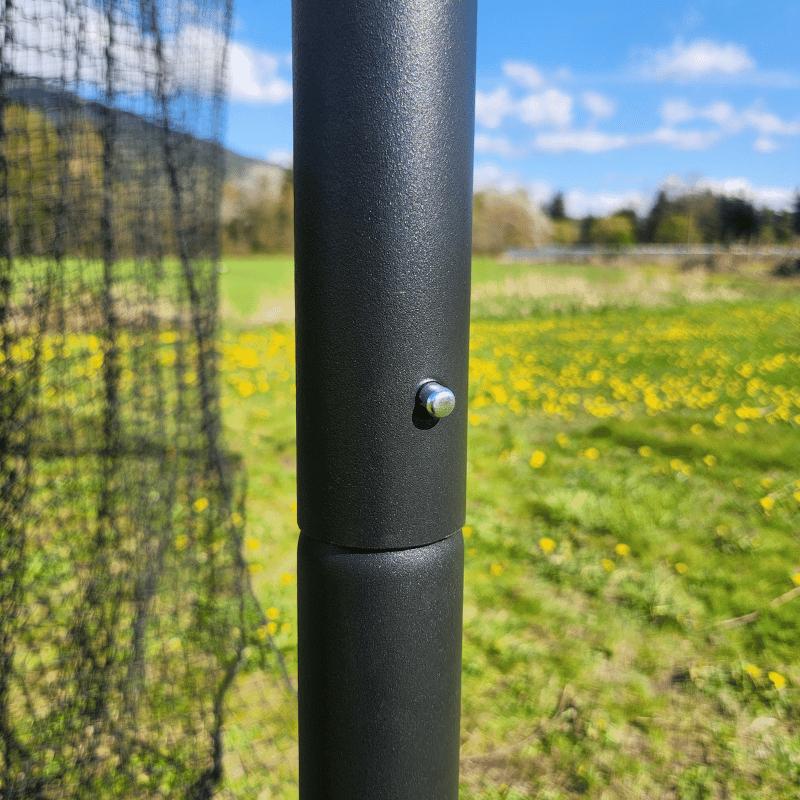 The Thumper Batting Cage pole with netting, grass, and blue skys behind