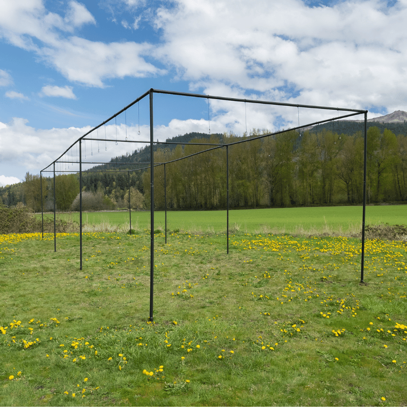 The Thumper Batting Cage Frame Kit with green grass, hills, and blue skies above