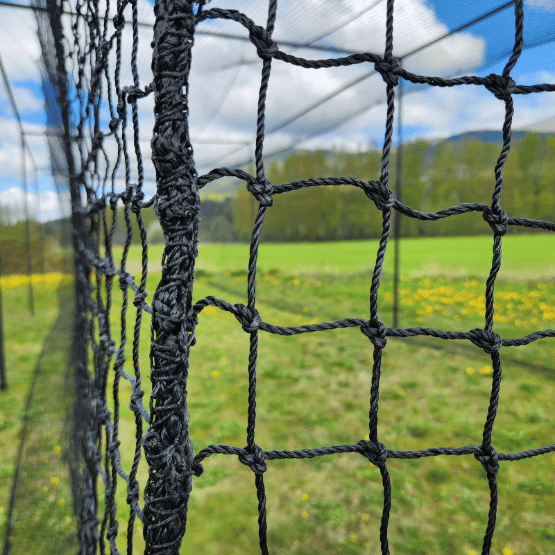 #24 HDPE Batting Cage Net close up of the netting meshes with green grass and blue cloudy skys