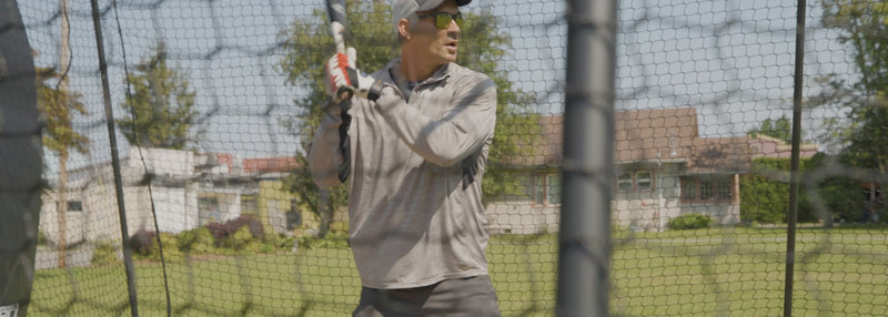 Man in trapezoid batting cage hitting baseballs